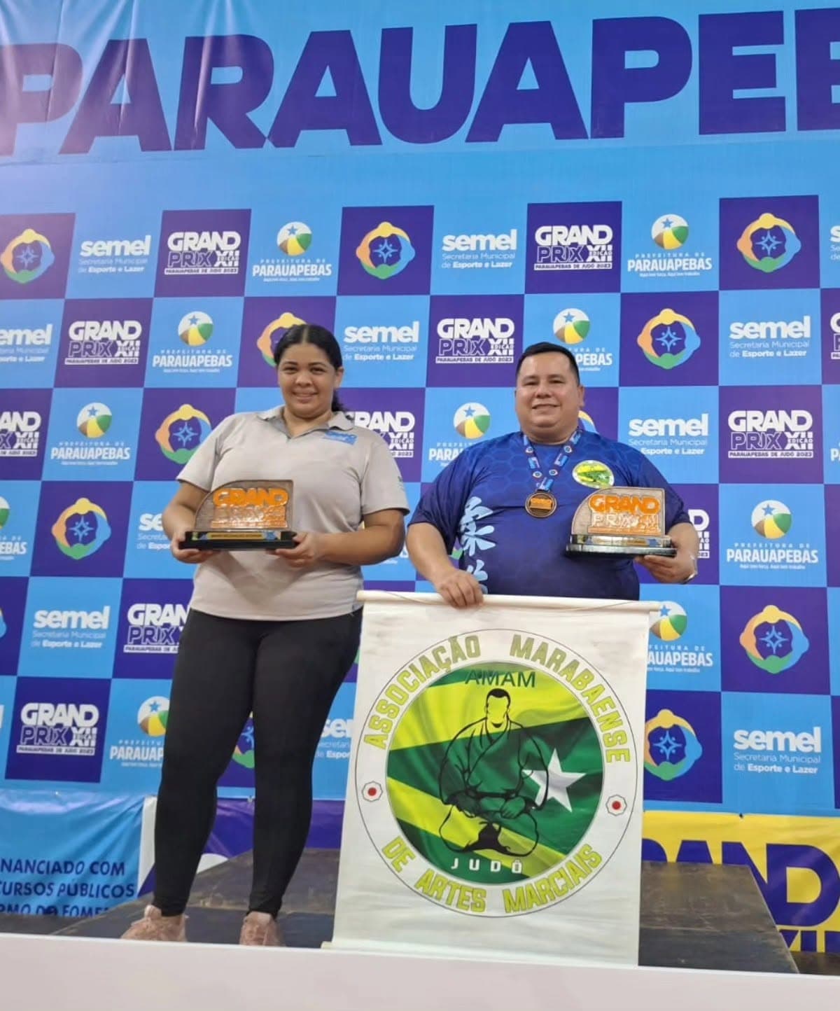 Pódio no Grand Prix de Parauapebas com troféus e o banner da AMAM