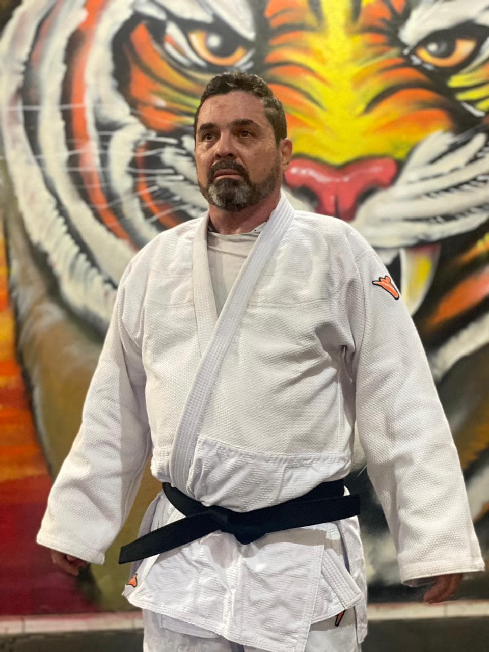 Mestre faixa preta da AMAM em kimono diante do grafite de tigre